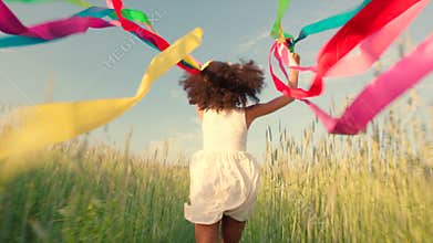 Young girl running with colored ribbons in her hands through the wheat field