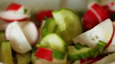 Stirring salad vegetables: radishes, cucumber, green onion, olive oil