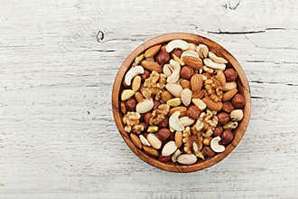 Wooden bowl with mixed nuts on white table from above. Healthy food and snack. Walnut, pistachios, almonds, hazelnuts and
