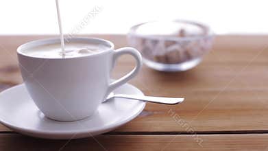 Cream pouring to coffee cup on wooden table