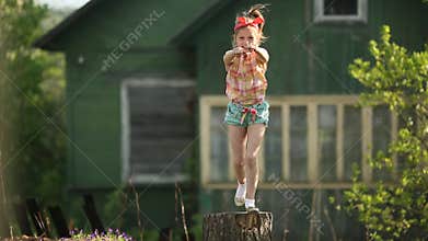 Little cute girl dancing on a stump in the yard of a country house. Happy.