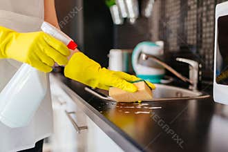 Woman cleaning kitchen cabinets with sponge and spray cleaner