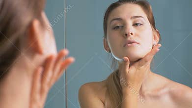 Portrait of young woman looking at mirror and checking her face