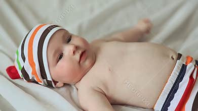 Funny four month old baby lying on his back and smiling. Dressed baby in striped shorts and cap