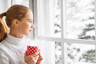 Happy young woman with cup of hot tea in winter window Christmas