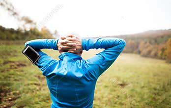 Senior runner with smartphone doing stretching. Autumn nature.