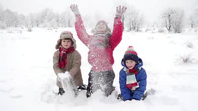 Three happy kids throwing snow on winter landscape, slow motion