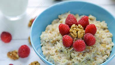 Healthy breakfast - oatmeal with fresh, ripe raspberries and walnuts in a bowl standing on a wooden table. Close up