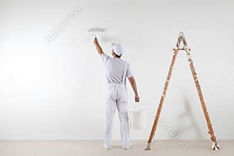 Rear view of painter man painting the wall, with paint roller an