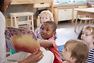 Pupils At Montessori School Looking At Book With Teacher