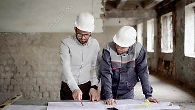 An adult engineer explains to the worker a new construction plan, which was designed by the architect, people are in an