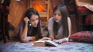 Closeup shot of two girls in pajamas reading fairytale book in bedroom at night