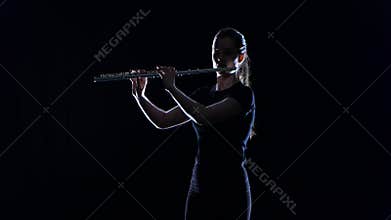 Female musician blows the motif in flute on black studio