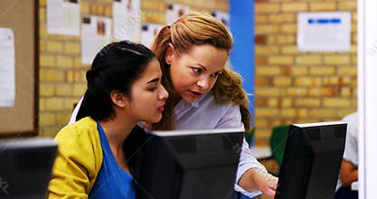 Teacher assisting schoolgirl in computer class