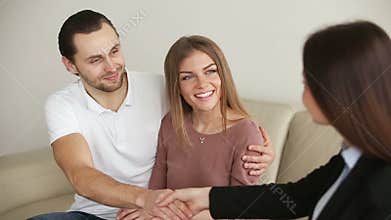 Young happy couple shaking hands with broker