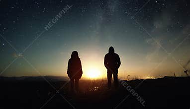 A couple of people man and woman stand at the sunset of the moon under the starry sky with bright stars and a milky way