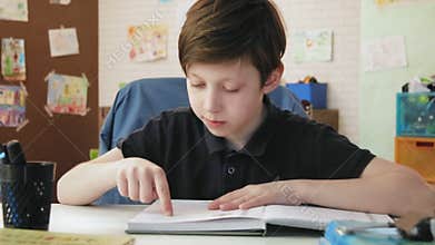 Cute little boy reading a book for school in his room