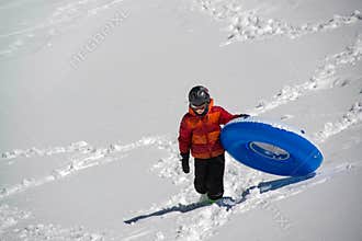 Teenage Boy carrying inflatable sledding tube up snowy hill in the mountains