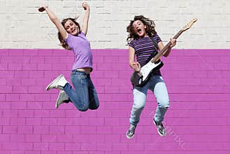 Teens playing guitar jumping