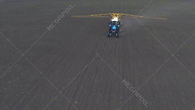 The tractor rides and sprays the fertilizer on the crop planted on the field, shooting from the air.