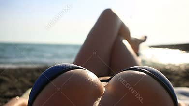 Young beautiful tanned girl in bikini lying on the beach by the sea. View of the sea through the female breast.