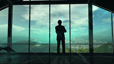 A man is standing by the window viewing IOT infographics elements