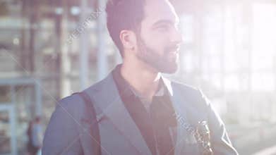 Gorgeous bearded man of Eastern appearance in luxurious outfit going out of the shopping center, joyfully looking around