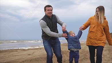 Young family enjoying walking on the beach. Man, woman little girl and boy