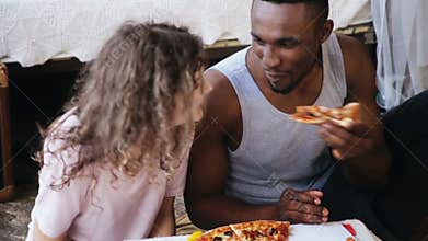 Hungry multiethnic couple eating pizza. Man and woman feeds each others, have fun during the meal with tasty fast food.
