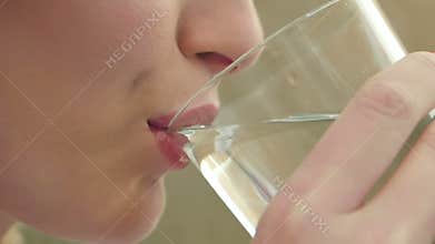 Gorgeous young girl is keeping healthy by drinking a glass of water indoors and smiling