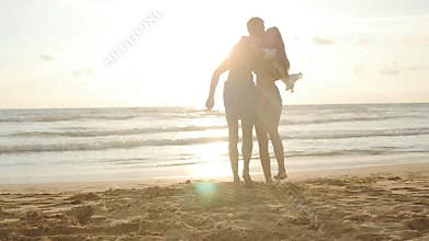Happy couple kissing and hugging each other at the sea beach at sunset. Young man and woman in love having fun together