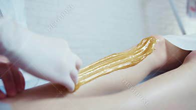 Beautician waxing woman`s leg in beauty spa