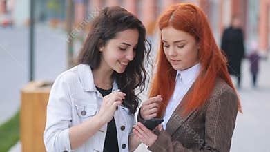 Young fantastic girls in business wear interested in something in smartphone, wind swaying the hair, positive moments