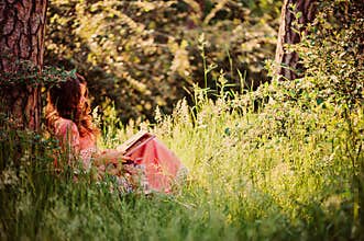 Summer portrait of happy child girl dressed in pink fairytale princess dress reading book