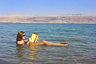 Young girl reads a book floating in the Dead Sea in Israel