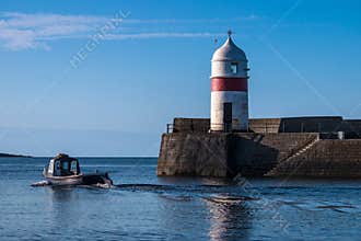 Fishing boat heading out to sea past harbor and lighthouse