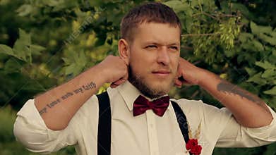 Groom wears a tie in the park at sunset