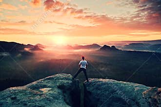 Crazy jumping hiker in black celebrate triumph between two rocky peaks above mist.. Wonderful autumn daybreak.