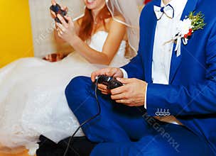 Bride and groom playing together videogames with joysticks - gaming and wedding concept.