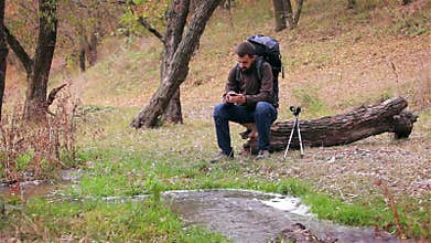 Man tourist with a backpack uses smartphone in the forest