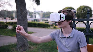 Young man with 3D VR head mounted display in park watching 360 movies, playing VR games.