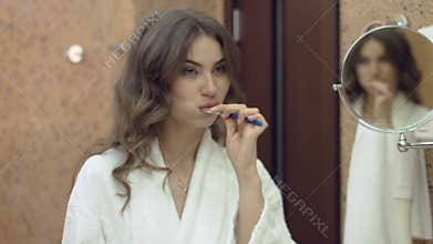 Beautiful woman in the bathrobe standing in the bathroom and brushes her teeth in the morning