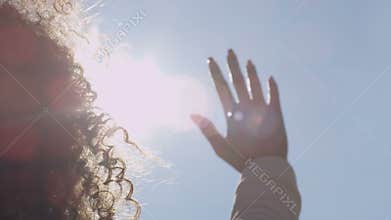 Female hand touching blue sky and raising to sun.