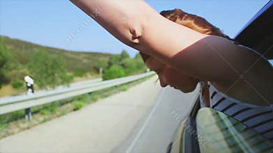 Young girl raise hands, scream out of open window of driving car. Wind. Smile. Traveling. Journey