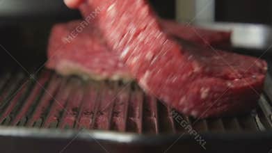 SLOW: Human hand puts a beefsteak on grill