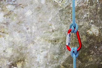 Red carabiner with climbing rope on rocky background