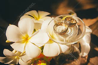 Bridal rings lay on glass near tropical flowers