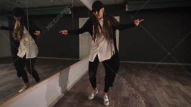 Young female dancer in white shirt, black trousers and black cap showing jazz modern dancing. Girl is dancing looking at