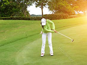 Smiling woman golf player putting successfully ball on green
