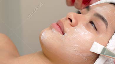 Beauty specialist uses brush to apply cosmetic mask on girl`s face